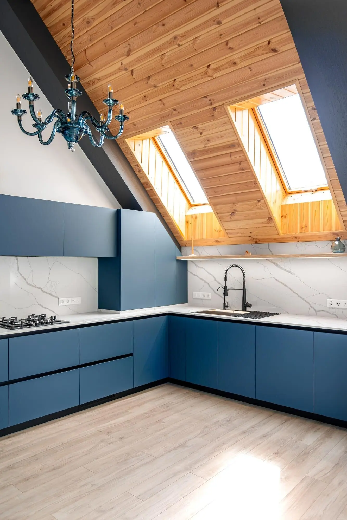 Cocina en ático con techo de madera y frentes azules modernos.
